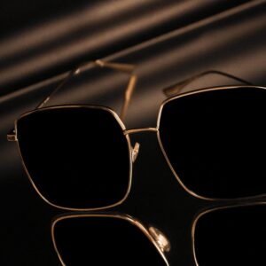 Shop Stylish square sunglasses with gold frames reflecting on a glossy surface.